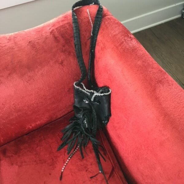 Black fringed purse with rhinestones on red couch.